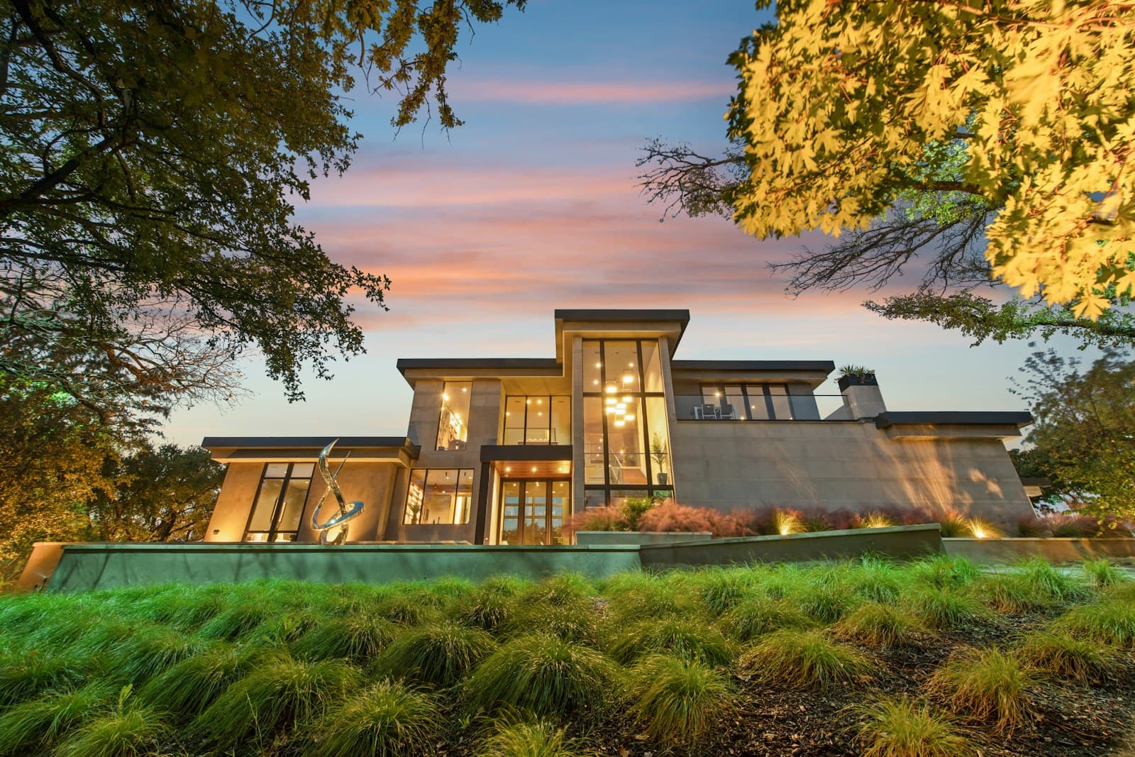 Casa contemporánea al atardecer con grandes ventanales y jardín de pastos